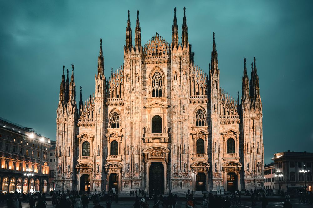 Gothic spires of Milan's Duomo cathedral stand majestically against a teal evening sky.