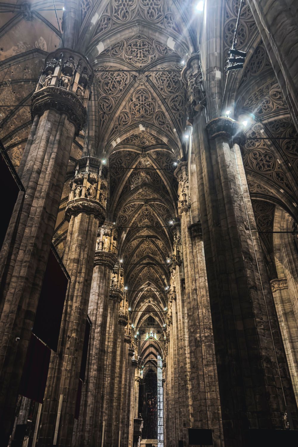 Dramatic interior view of Milan Cathedral's Gothic vaulted ceiling and stone columns.