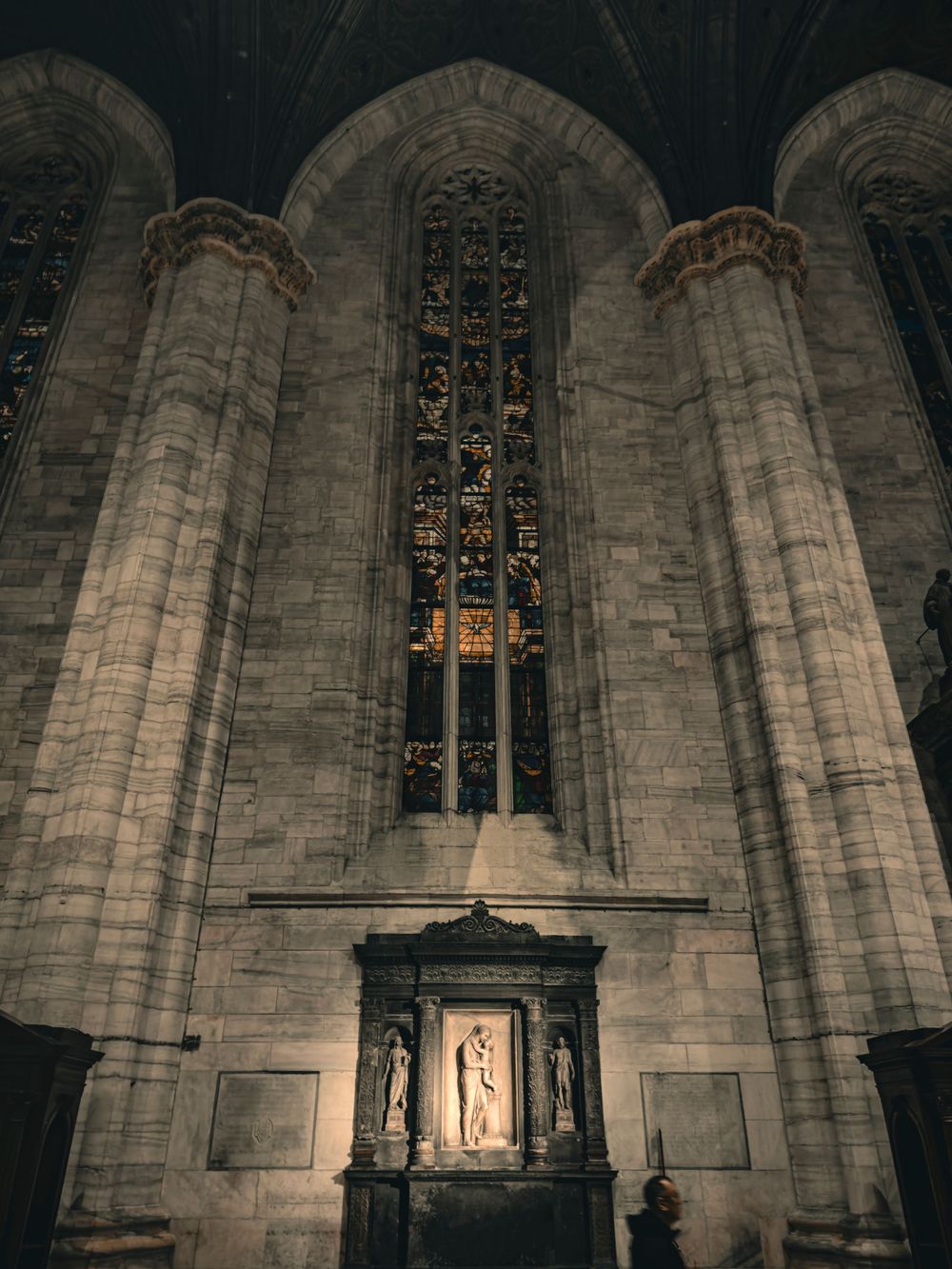 Historic church window with detailed Gothic stonework and ornamental religious artwork below.