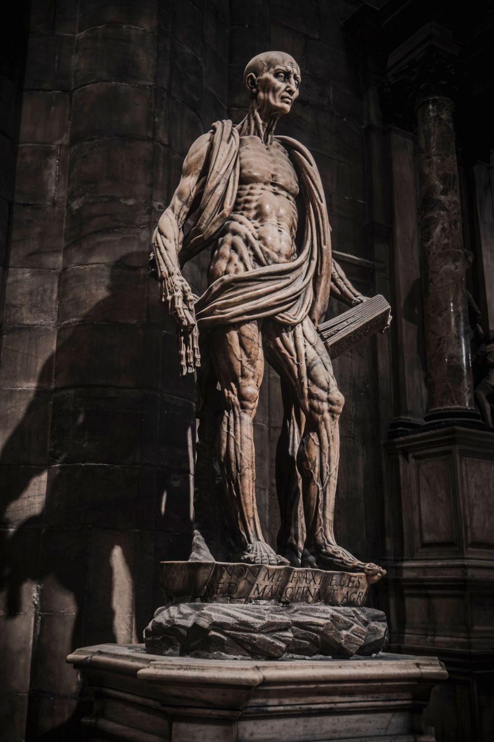 Dramatic statue of a skeletal figure in classical robes holding a book inside a gothic cathedral.