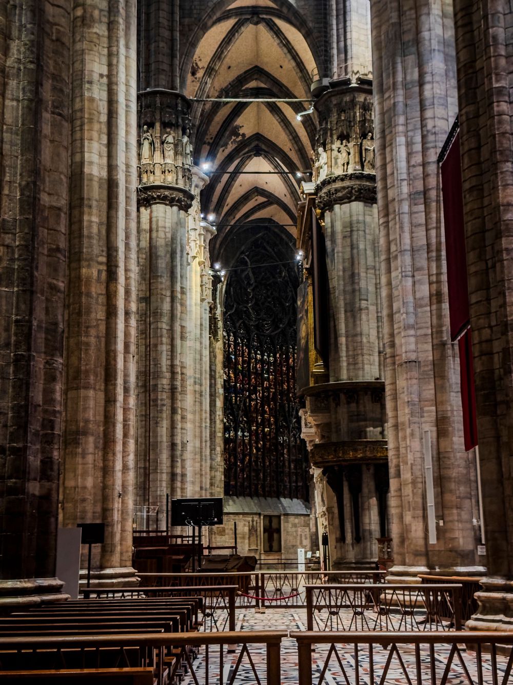 Gothic cathedral interior with pointed arches and stone columns leading to stained glass window.