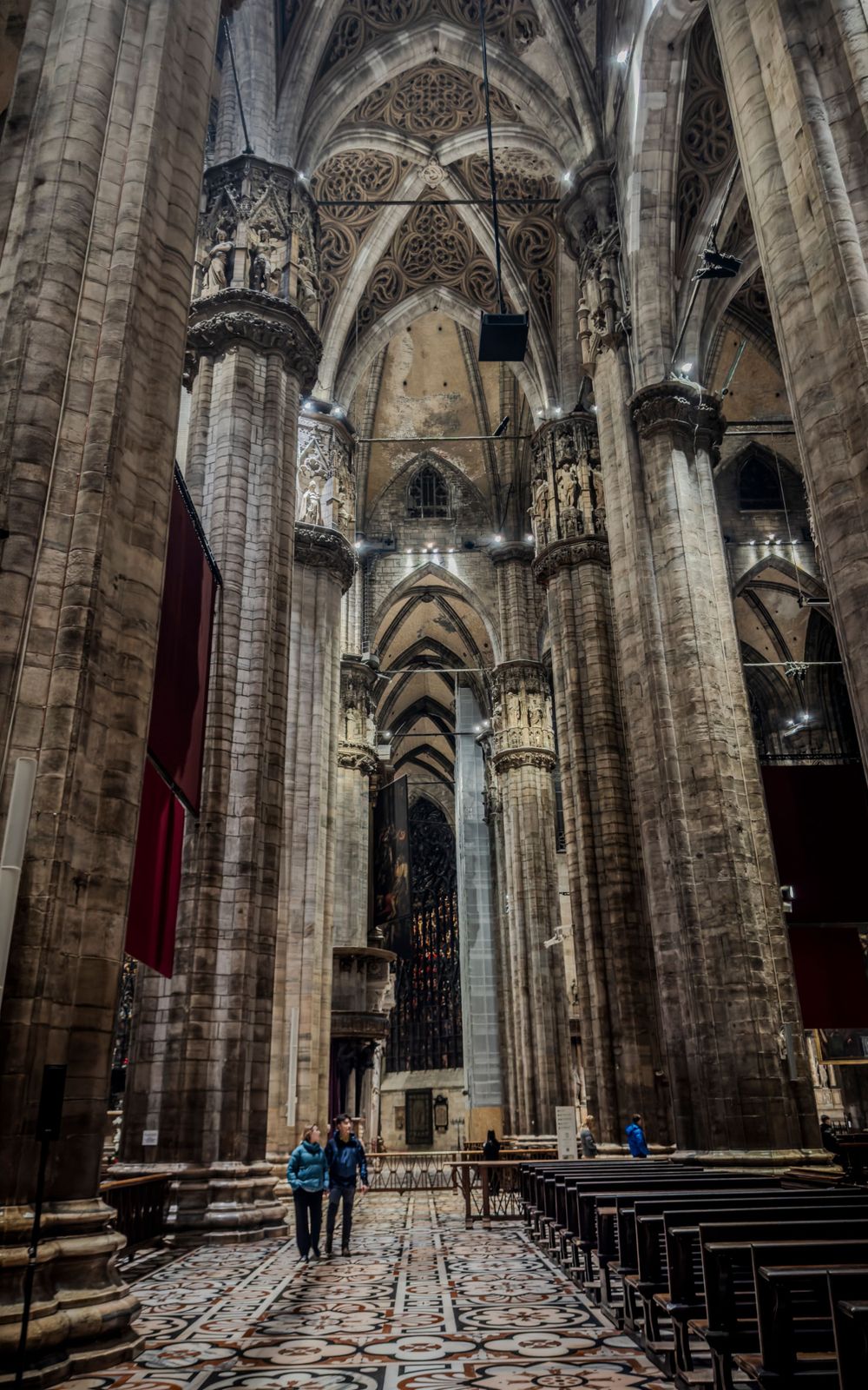 Towering gothic cathedral interior with massive stone columns and ribbed vaulting stretching toward the ceiling.