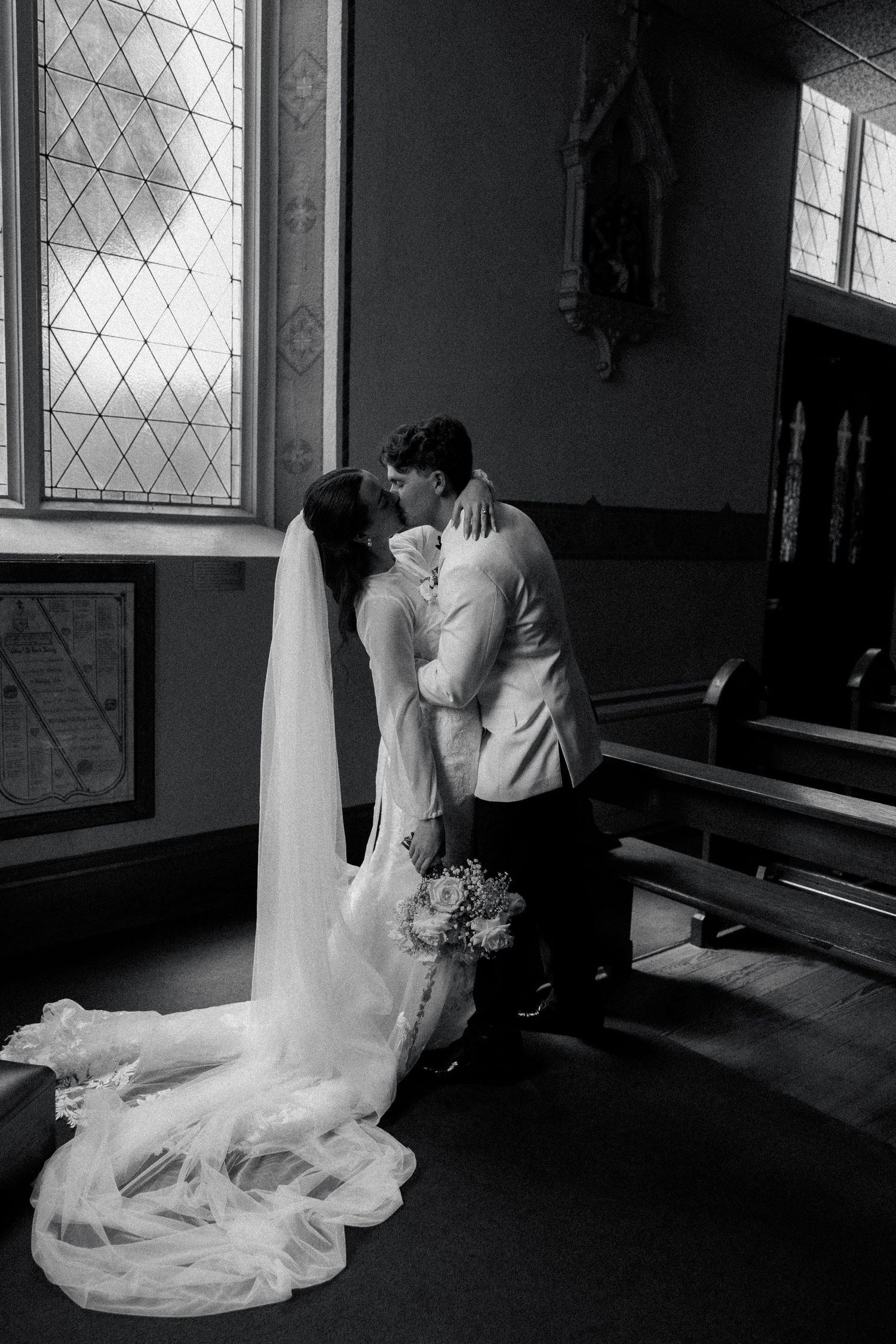 Black and white wedding photo capturing intimate moment by church window with flowing veil.