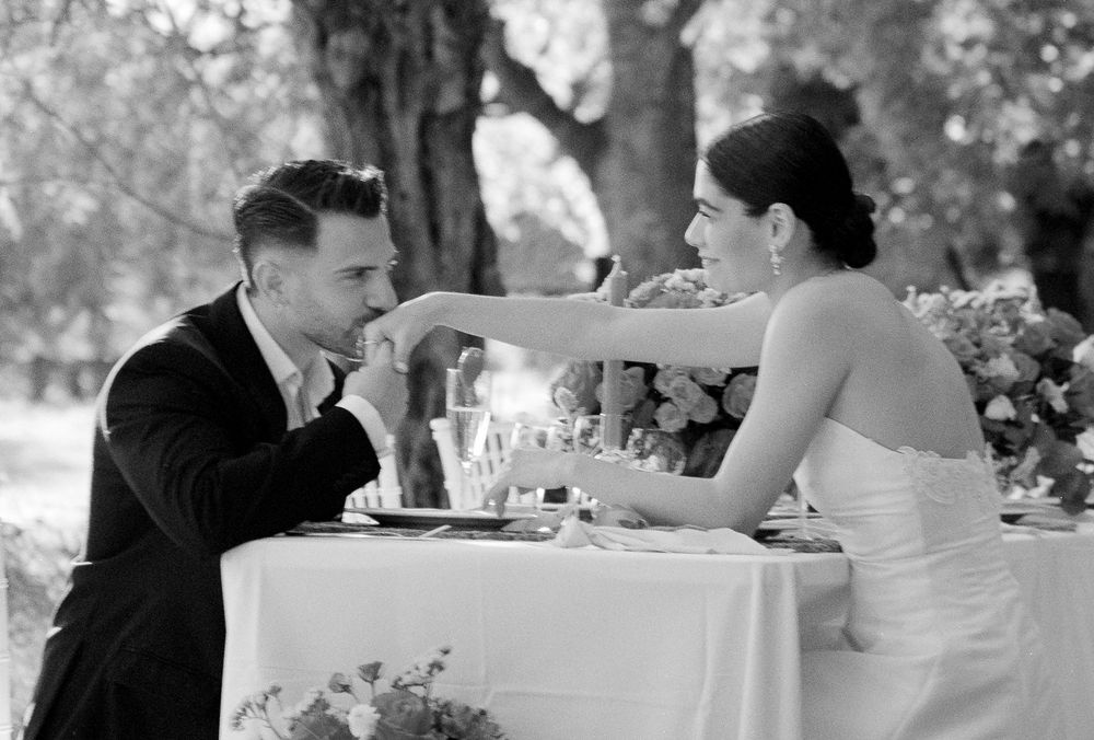 Groom kissing bride’s hand during an intimate wedding table moment in nature