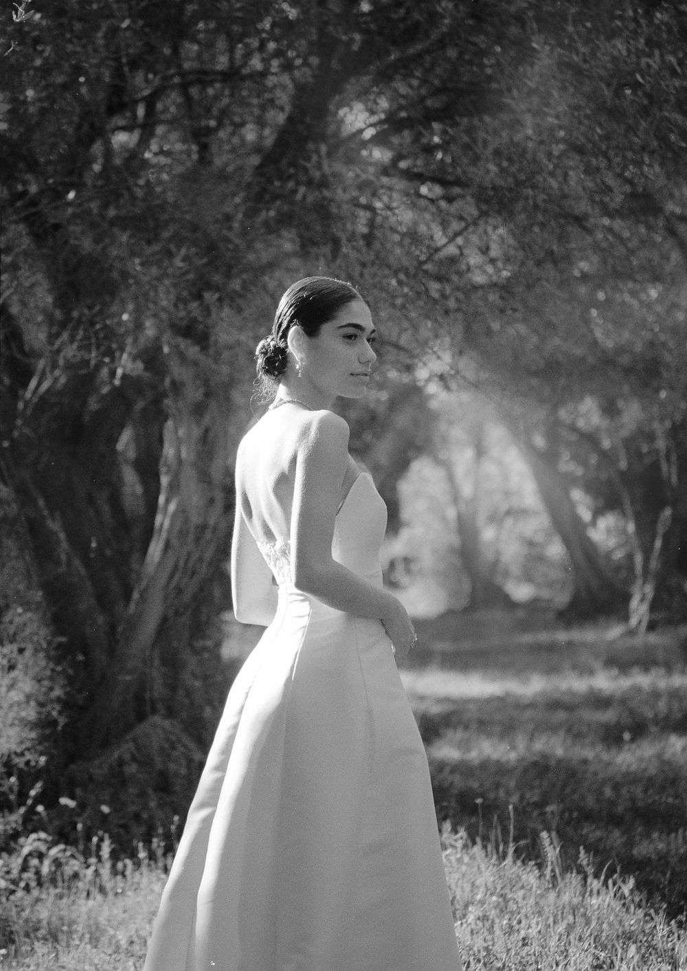 Bride in forest path turning softly toward the light in her wedding dress