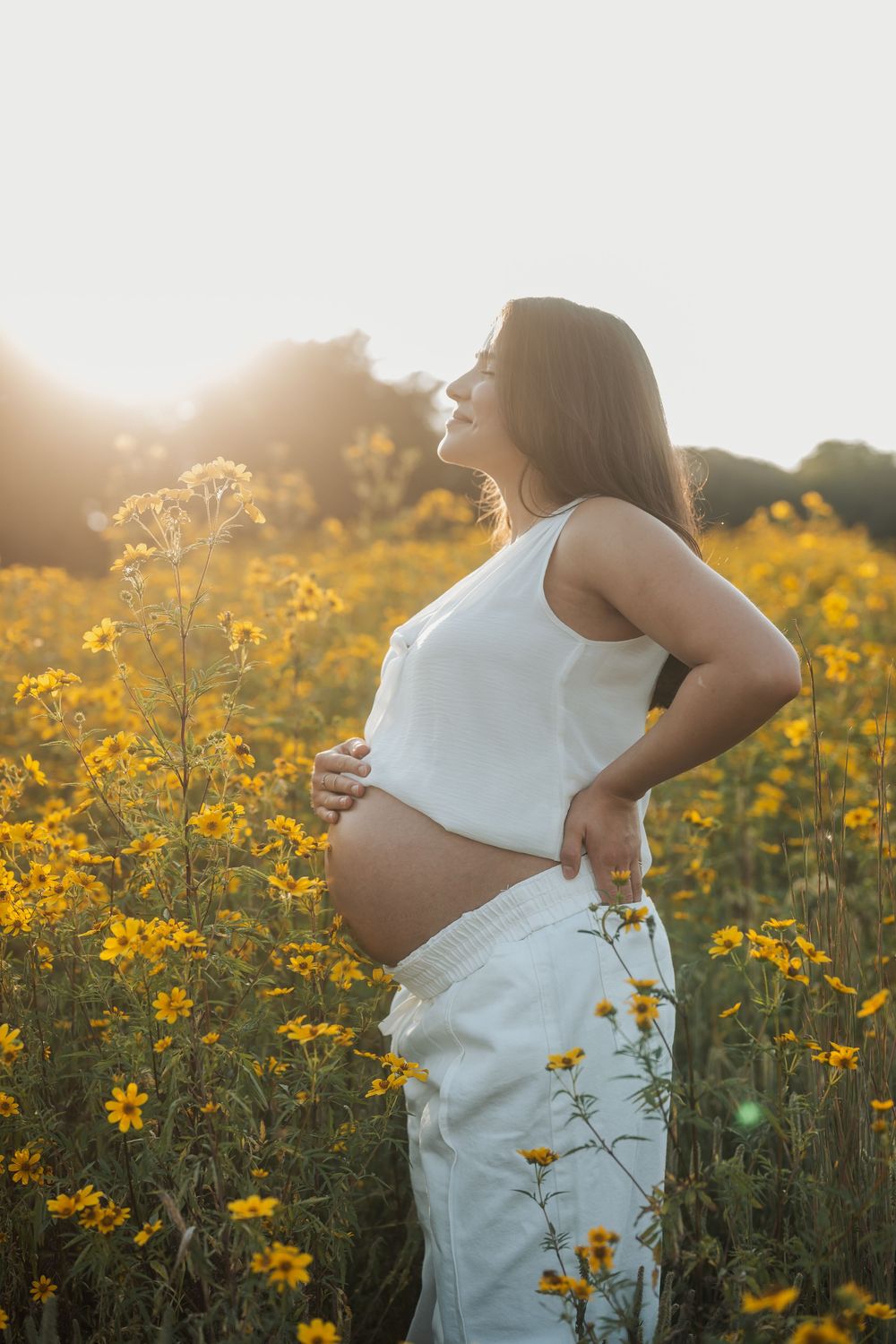 Silhouette of pregnant figure among yellow wildflowers at sunset.