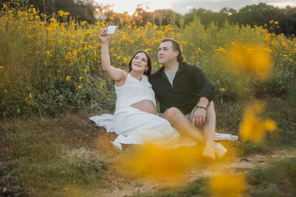Couple sharing tender moment in field of yellow wildflowers during maternity photoshoot.