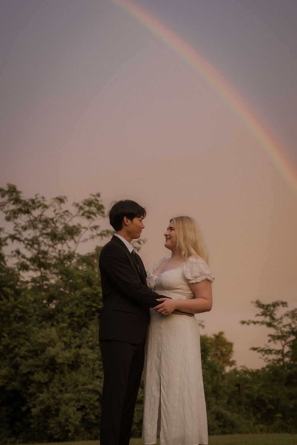 Rainbow arches over couple during sunset wedding photo session.