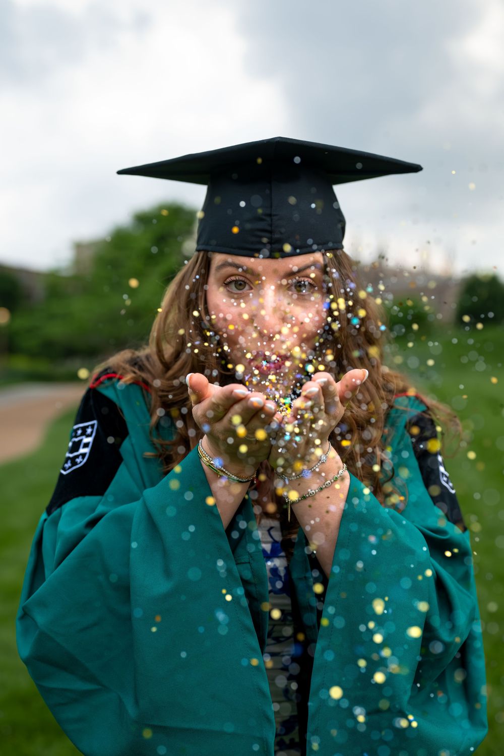 Celebratory moment with confetti and graduation cap against cloudy sky.