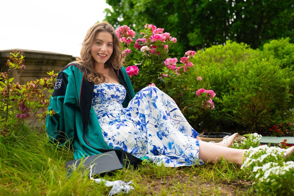 Graduate poses gracefully among blooming flower garden in blue and white dress.