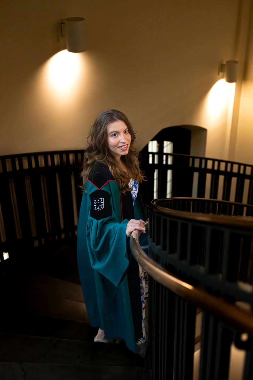Dramatic indoor portrait featuring graduation attire in warmly lit hallway.