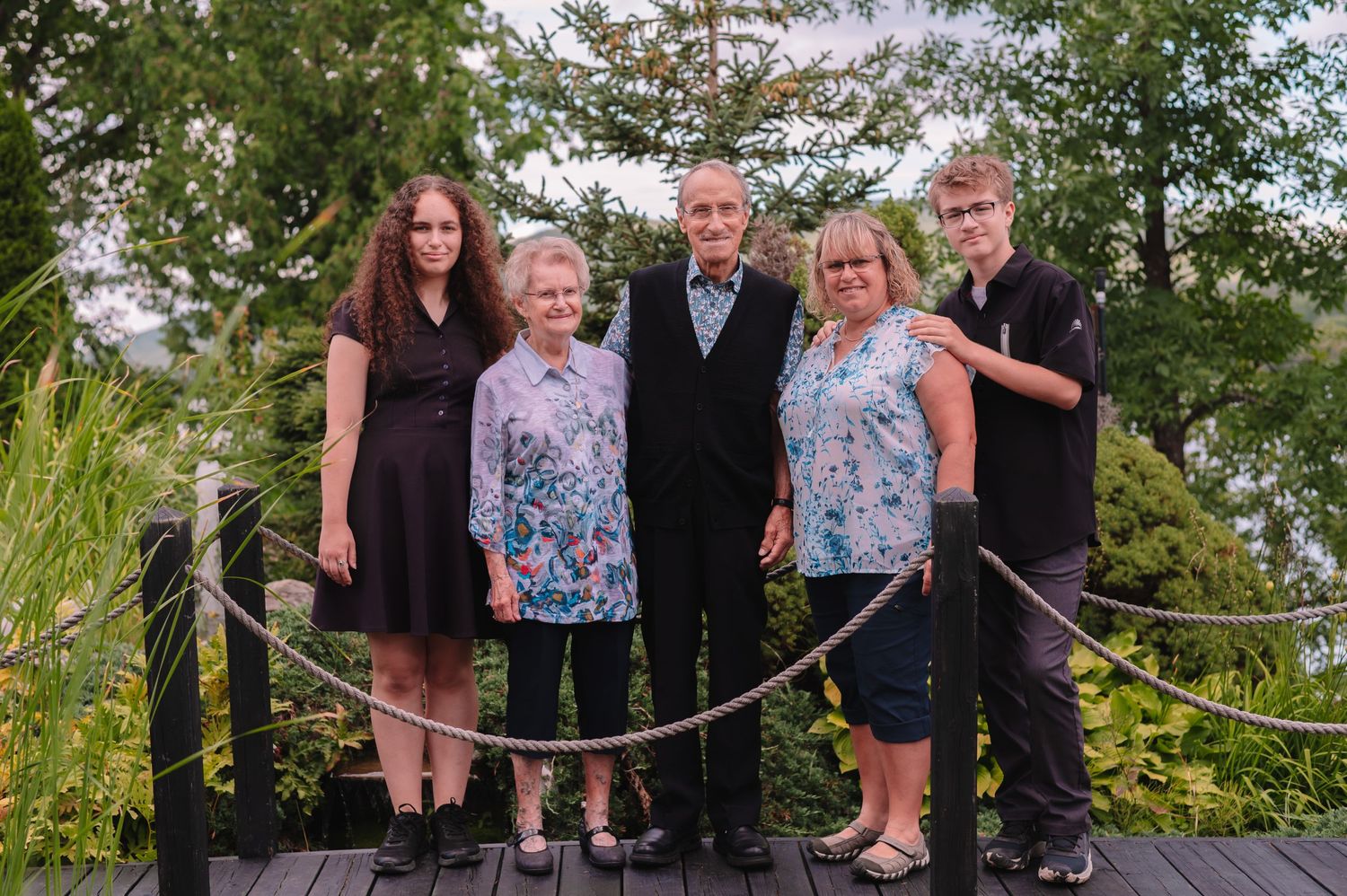 Group portrait of five people standing together on a wooden deck surrounded by greenery.