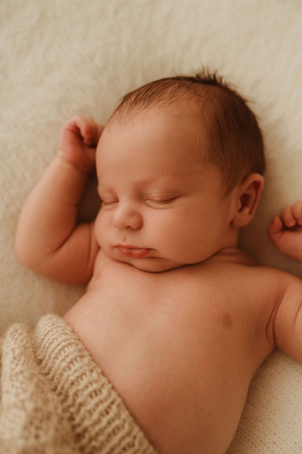 A sleeping newborn baby lies peacefully on soft white fabric in a series of connected photos.