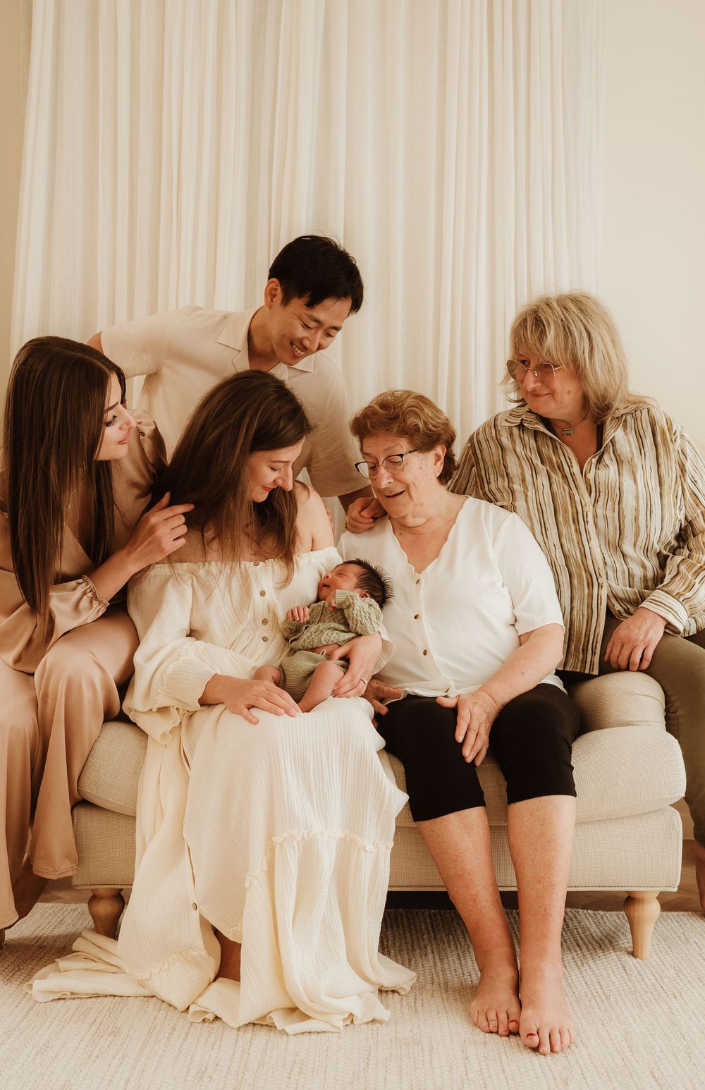 Family members sharing joyful moment while admiring newborn baby on couch.