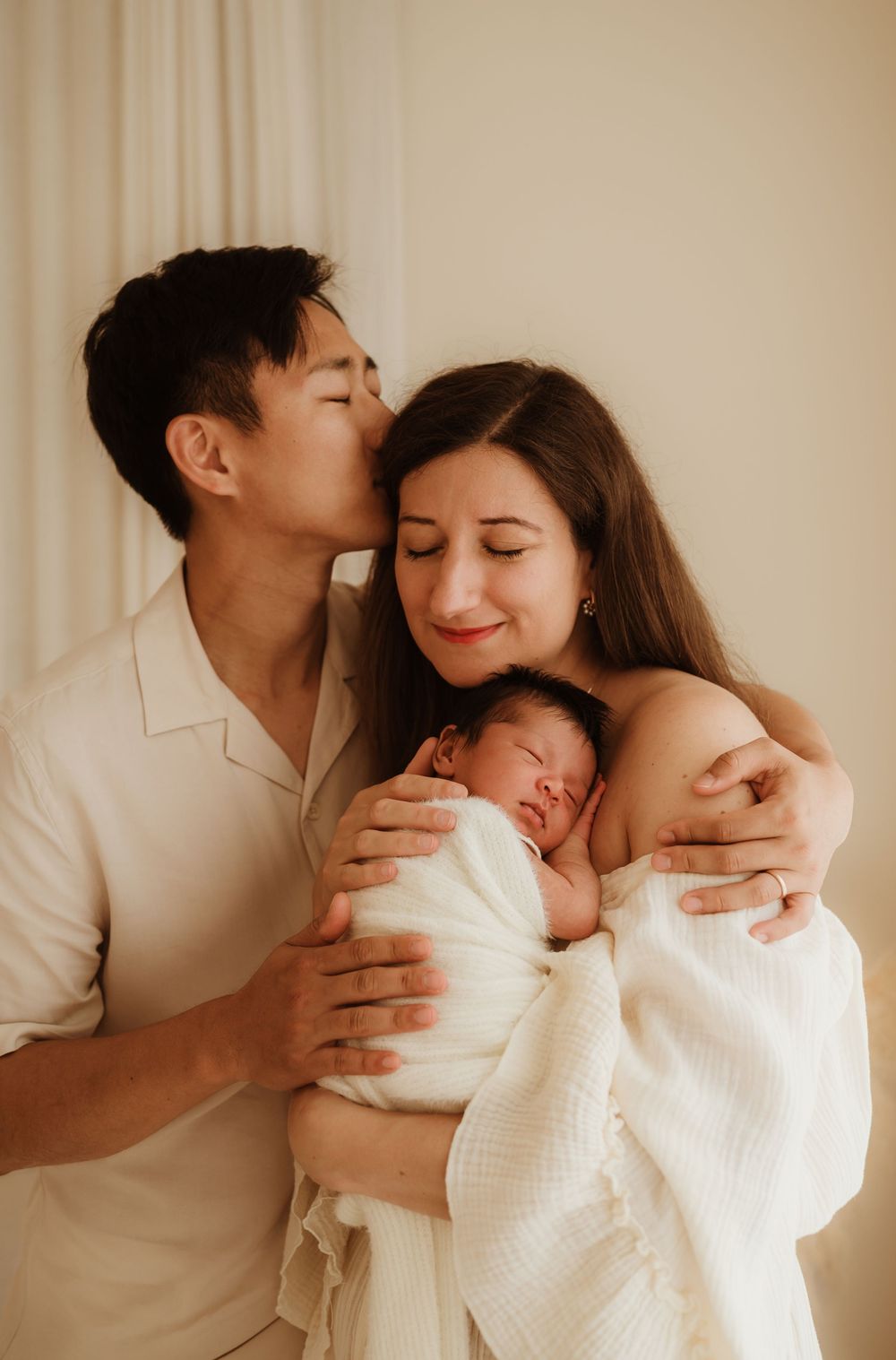 An intimate family moment captured in warm tones as they embrace their newborn baby.