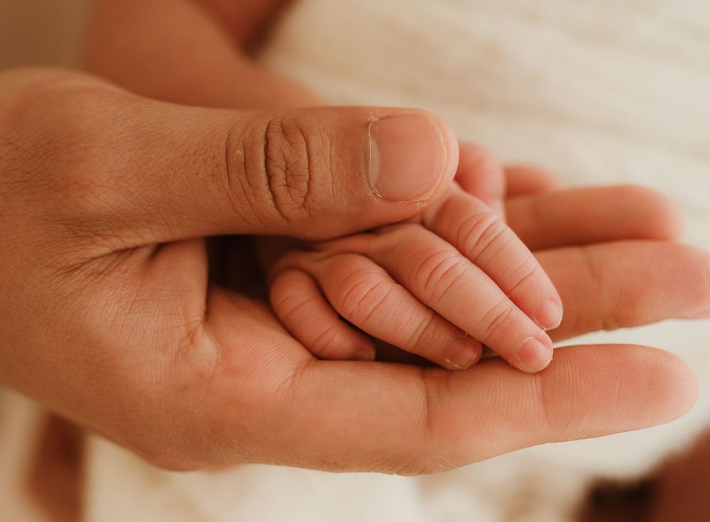 A tender close-up of two hands touching, one small and one large, representing a gentle moment of connection.