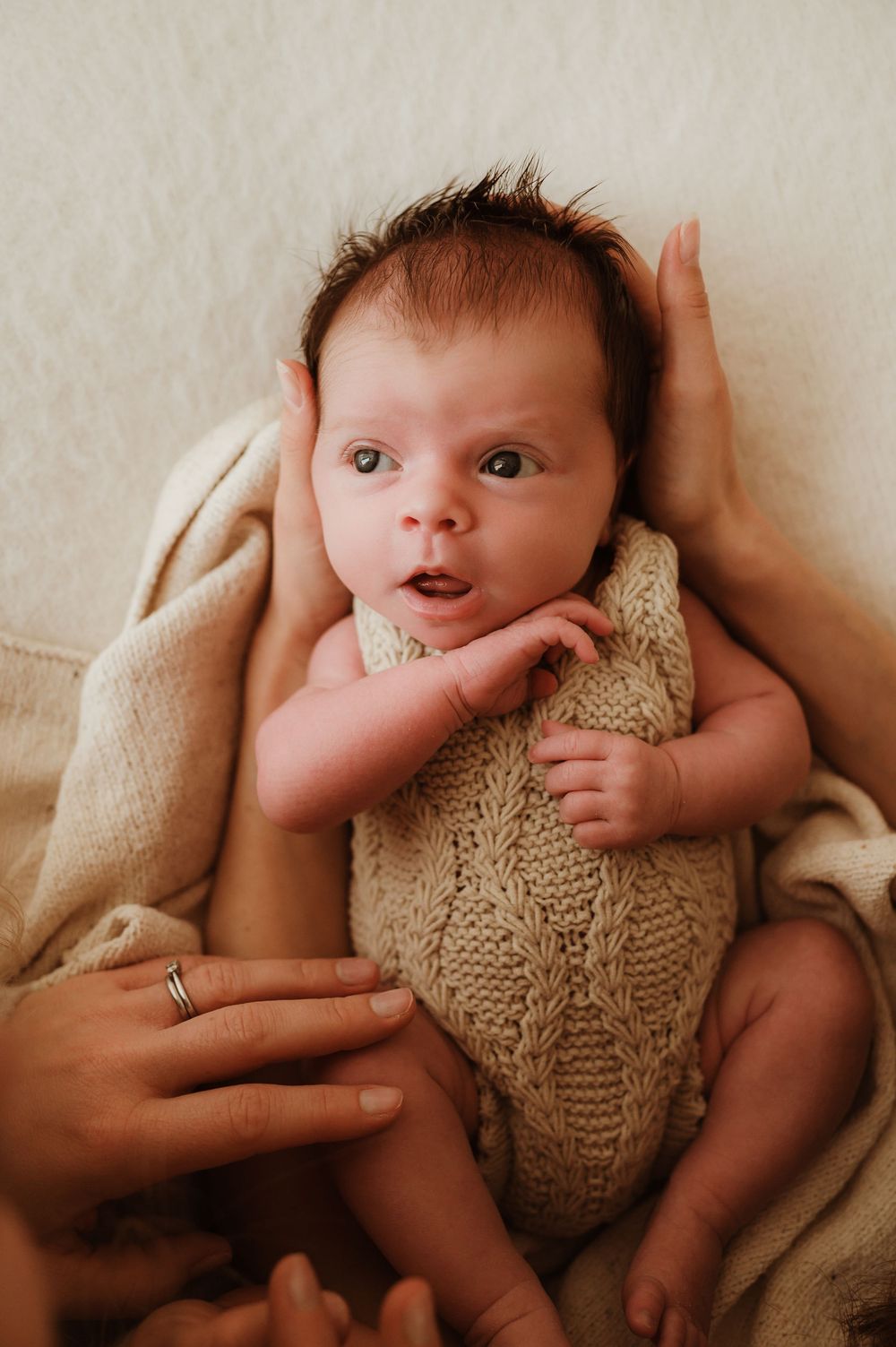 A series of photos showing a baby lying on cream-colored fabric wearing a knitted beige sweater in different poses.