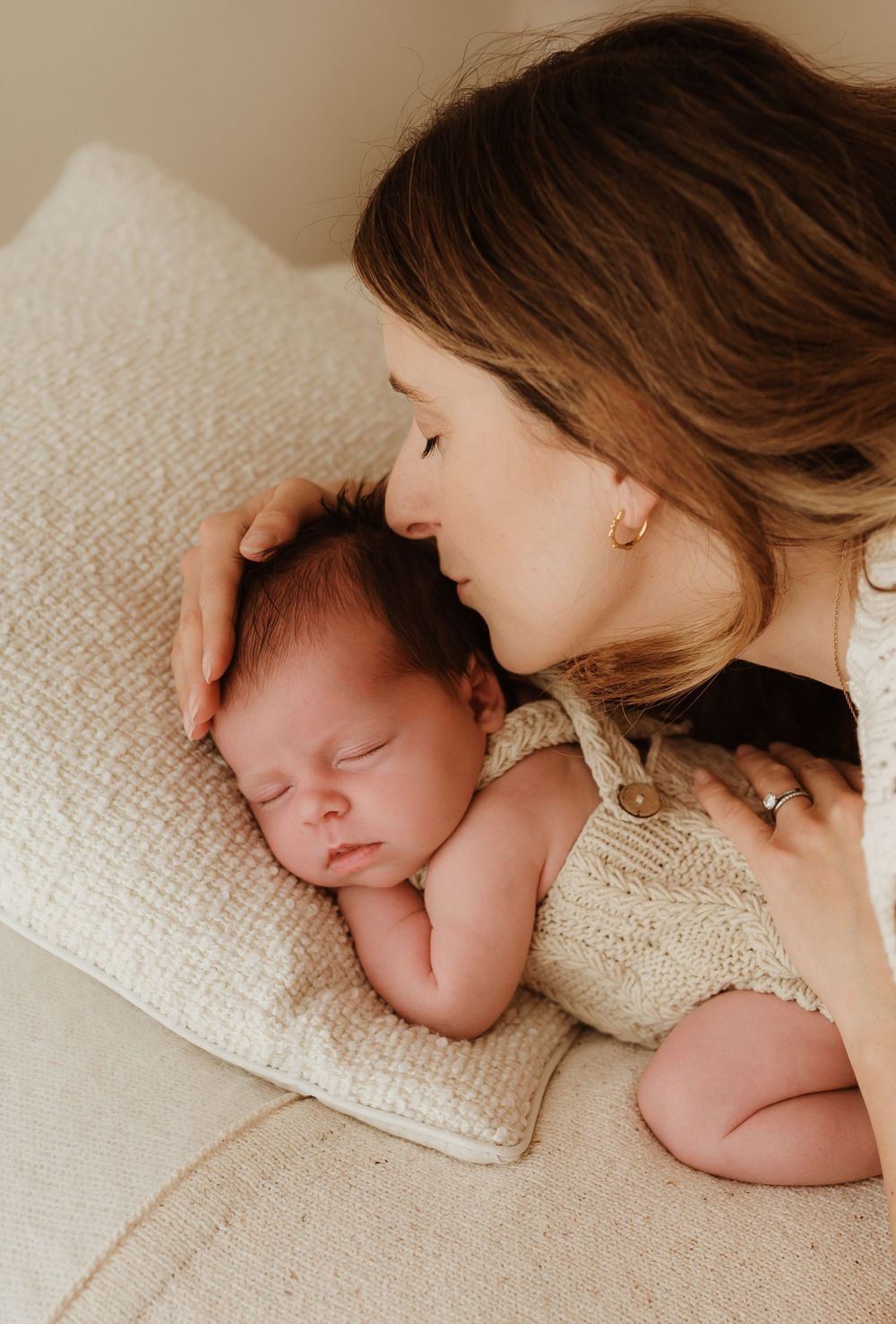 A tender moment captured as a mother gently embraces her sleeping newborn baby on a soft white blanket.