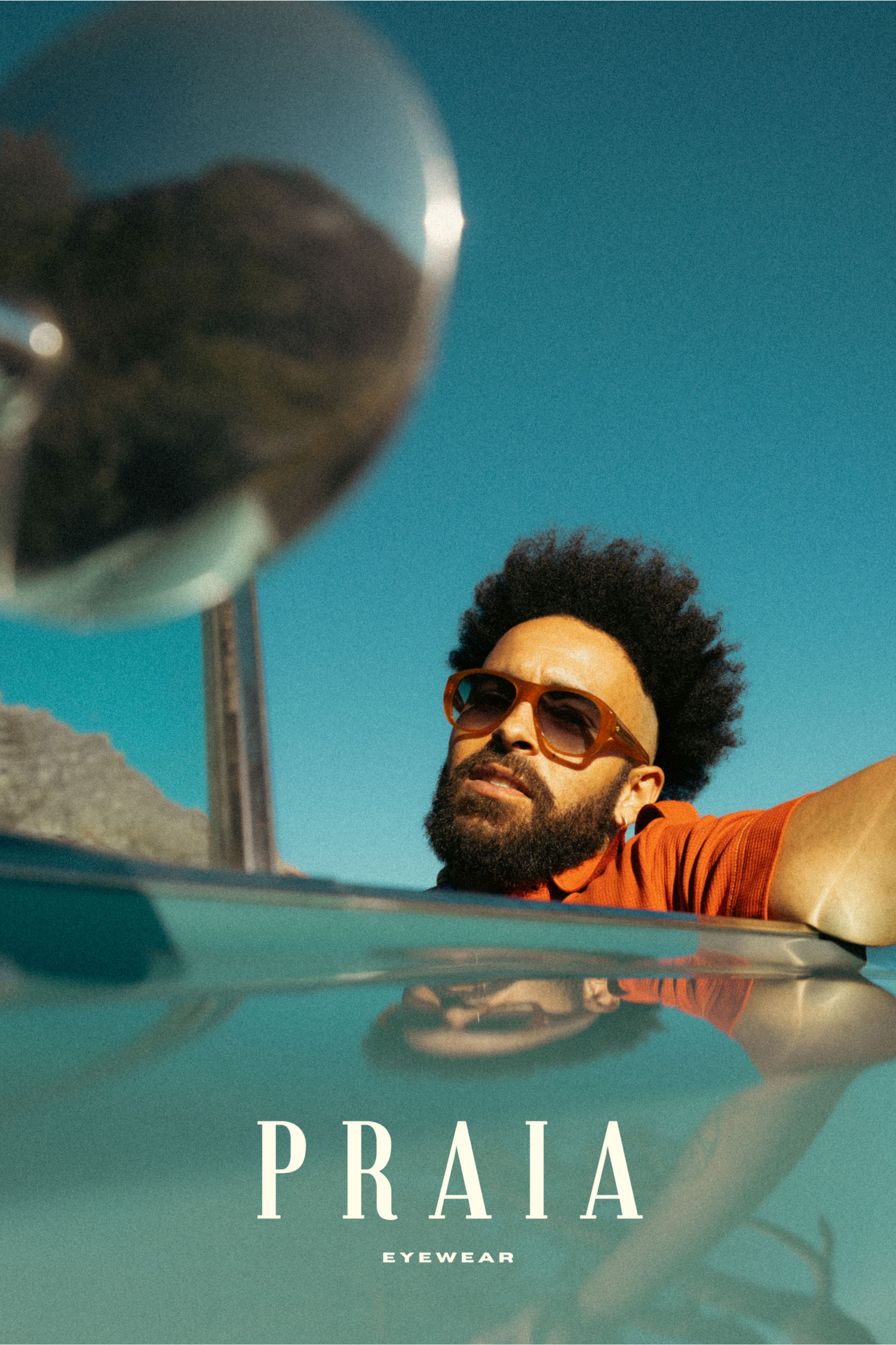 Contemporary sunglasses advertisement featuring model in orange shirt against blue sky with reflective surface.