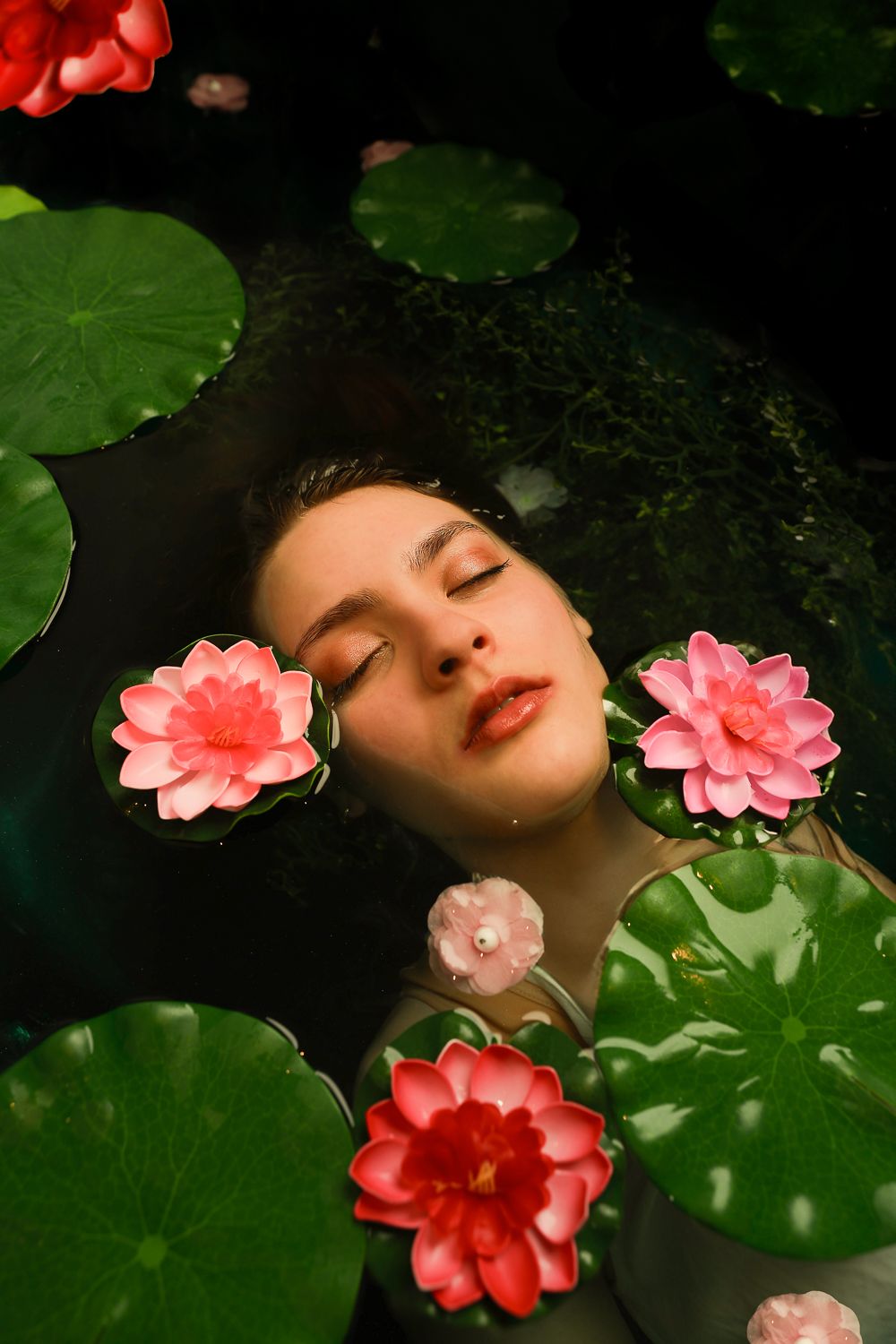 Girl in water surrounded by a dark green pond setting, eyes closed