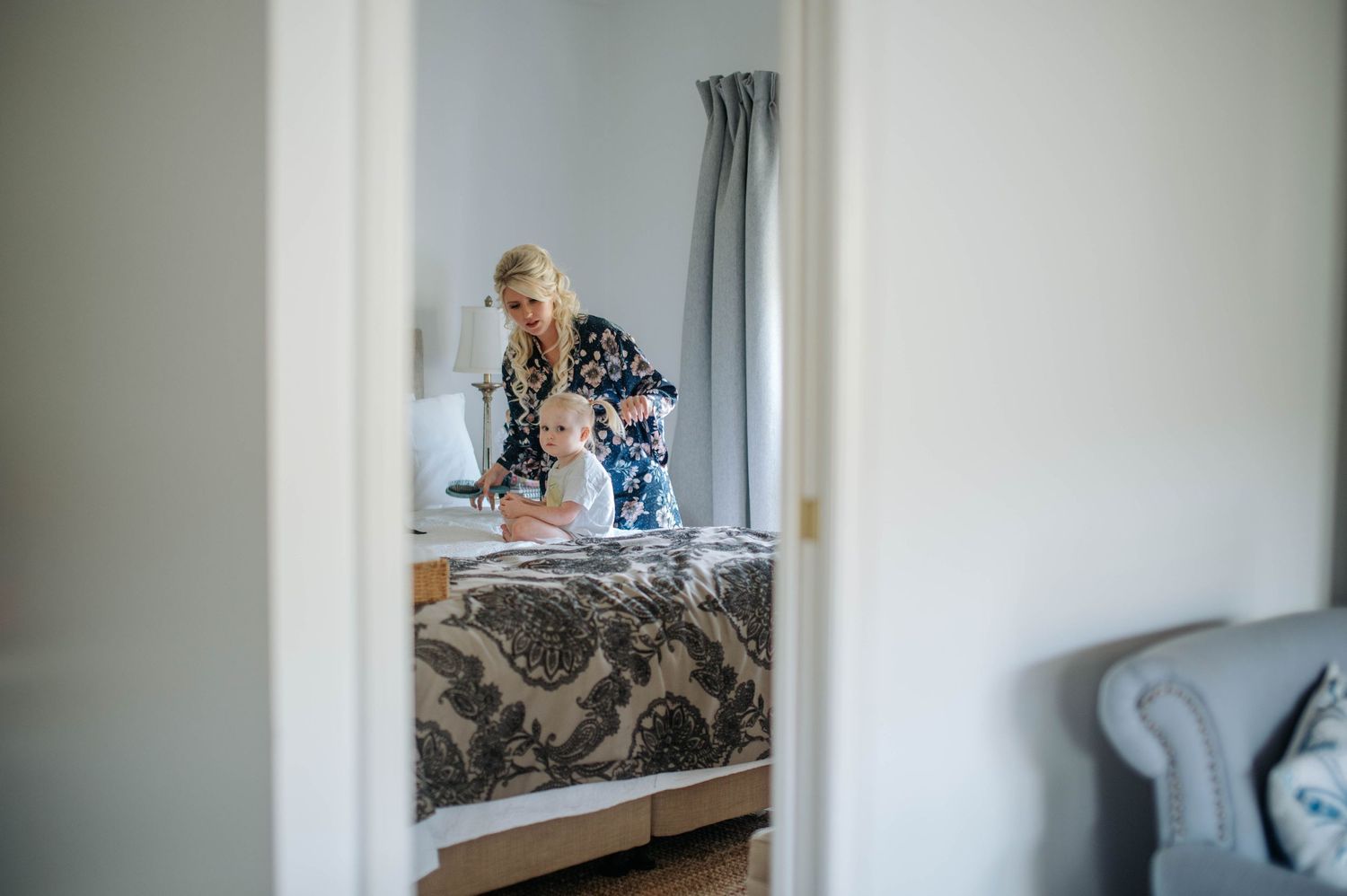 Getting ready scene through doorway with person at vanity in elegant bedroom.
