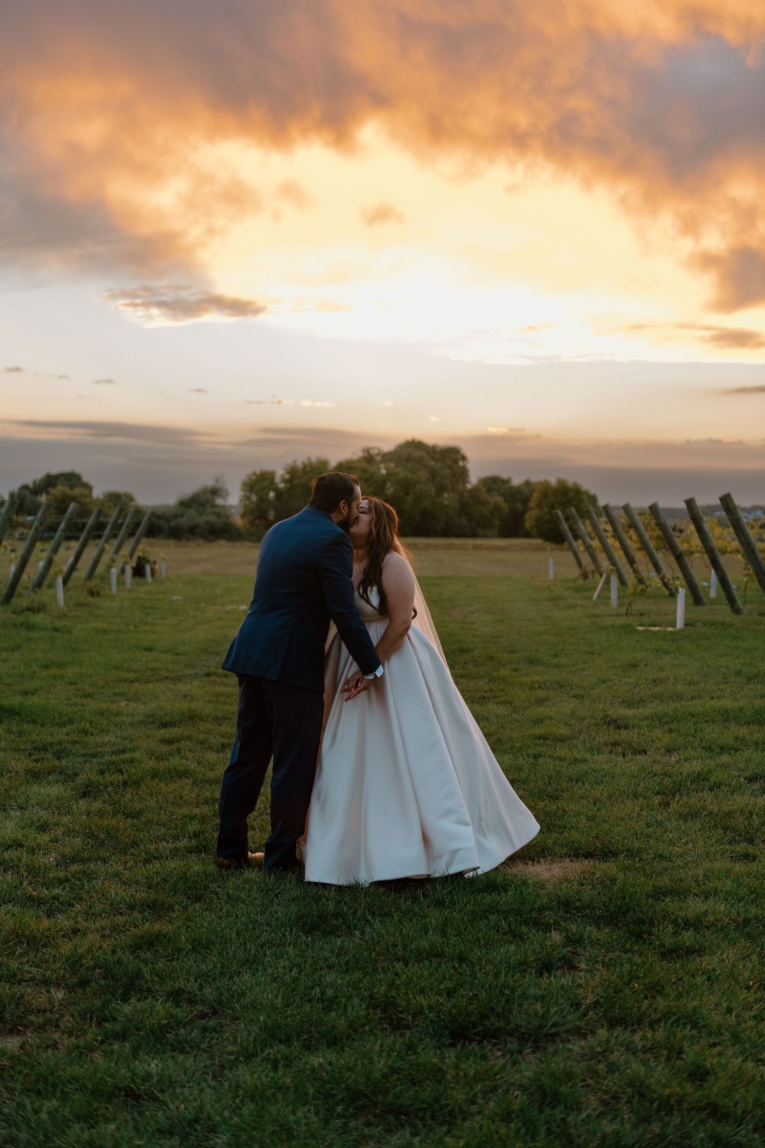 A couple shares an intimate moment at sunset in a field with solar panels under a dramatic orange sky.