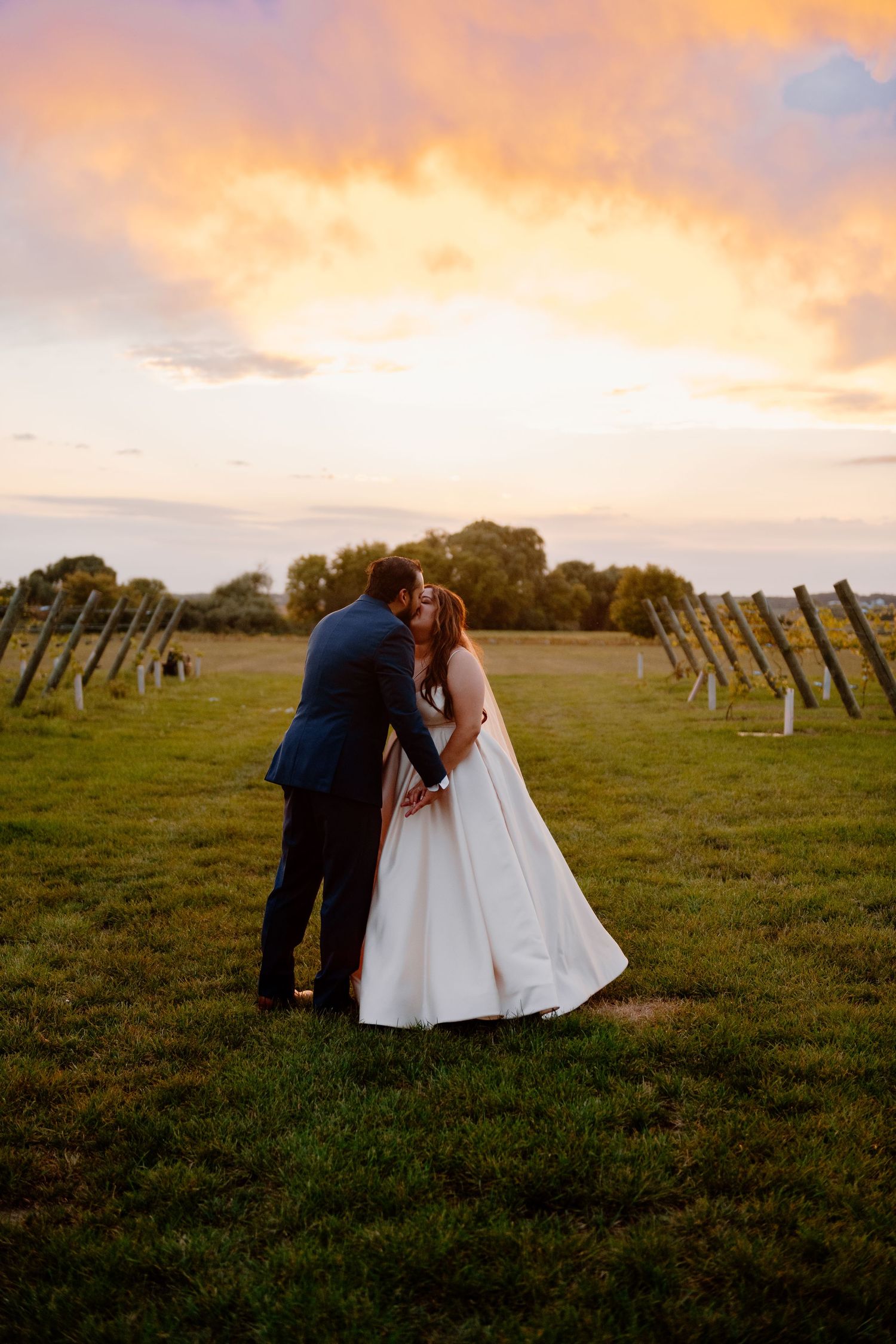 A couple shares an intimate moment at sunset in a field with solar panels under a dramatic orange sky.