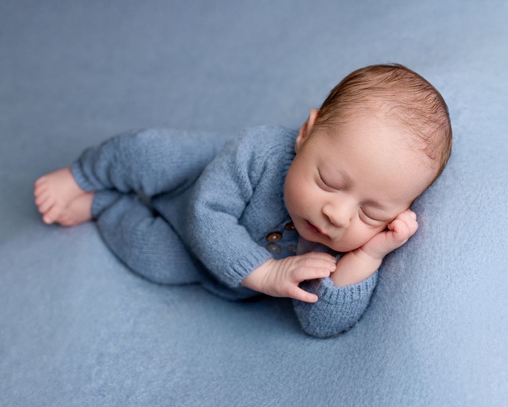 A sleeping infant wearing a cozy gray sweater lies peacefully on soft blue fabric.