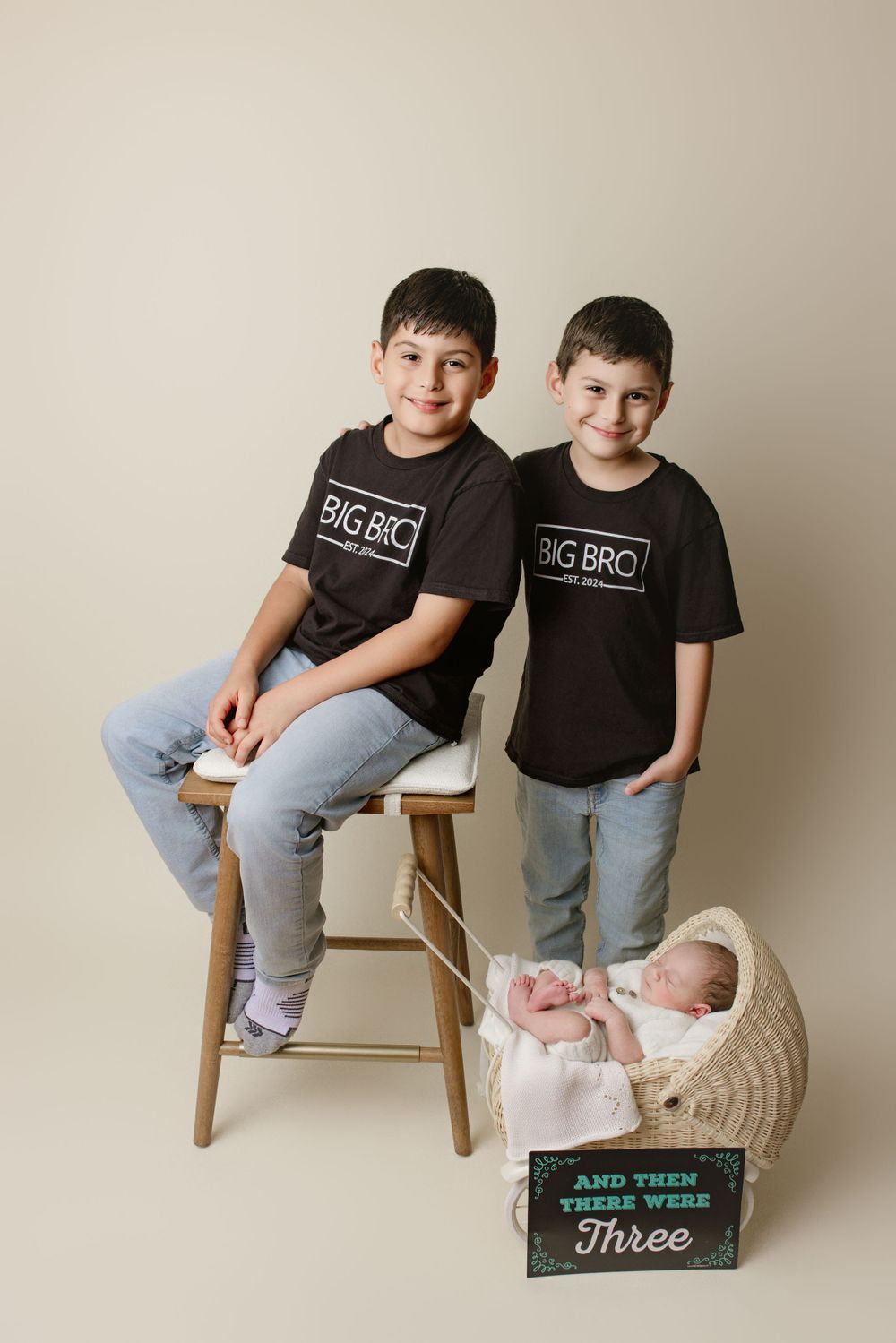 Studio portrait of siblings wearing matching black t-shirts with two sleeping newborn twins in basket below.