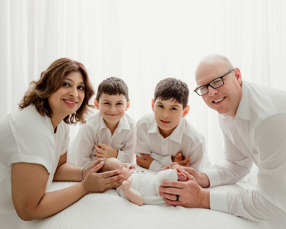 Family wearing white clothes lying together on light background for professional portrait session.
