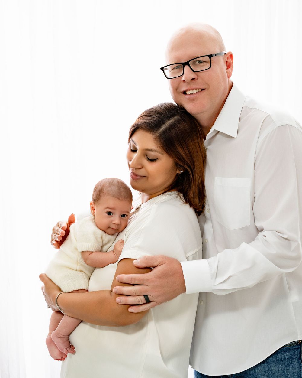 A family in matching white outfits sharing a tender moment together against a white background.