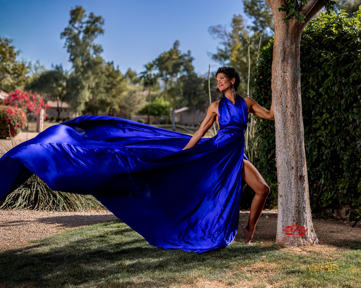 A woman wearing a blue eternity dress near an urban fountain with palm trees.