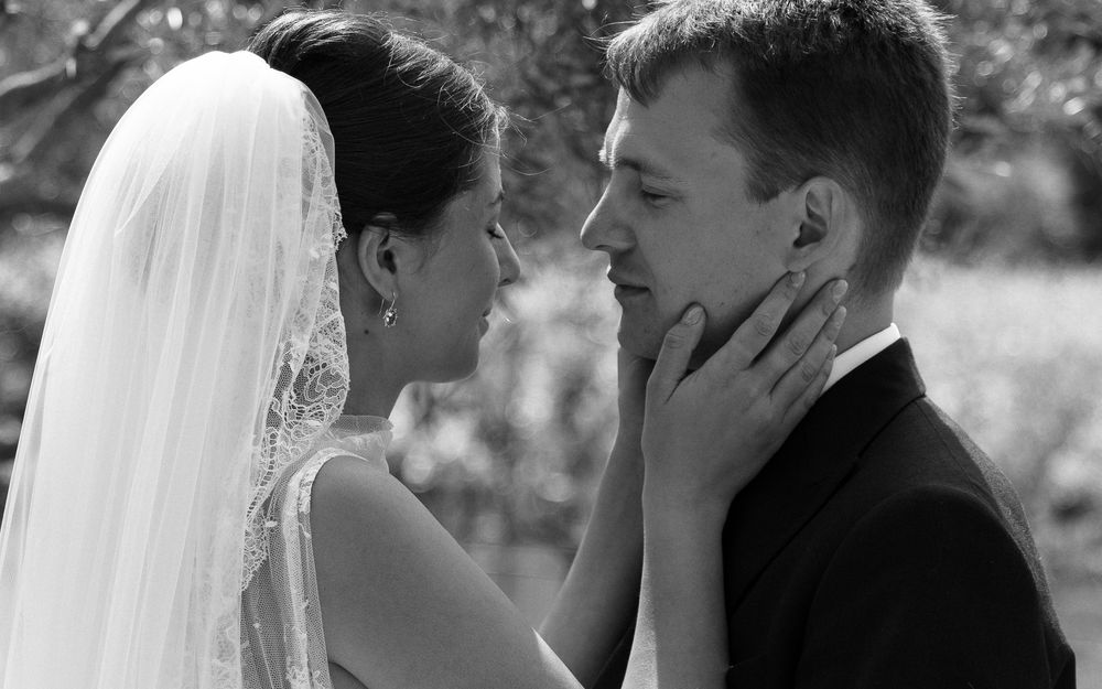 Black and white photo of a bride and groom sharing a tender moment, with the bride gently touching the groom's face.