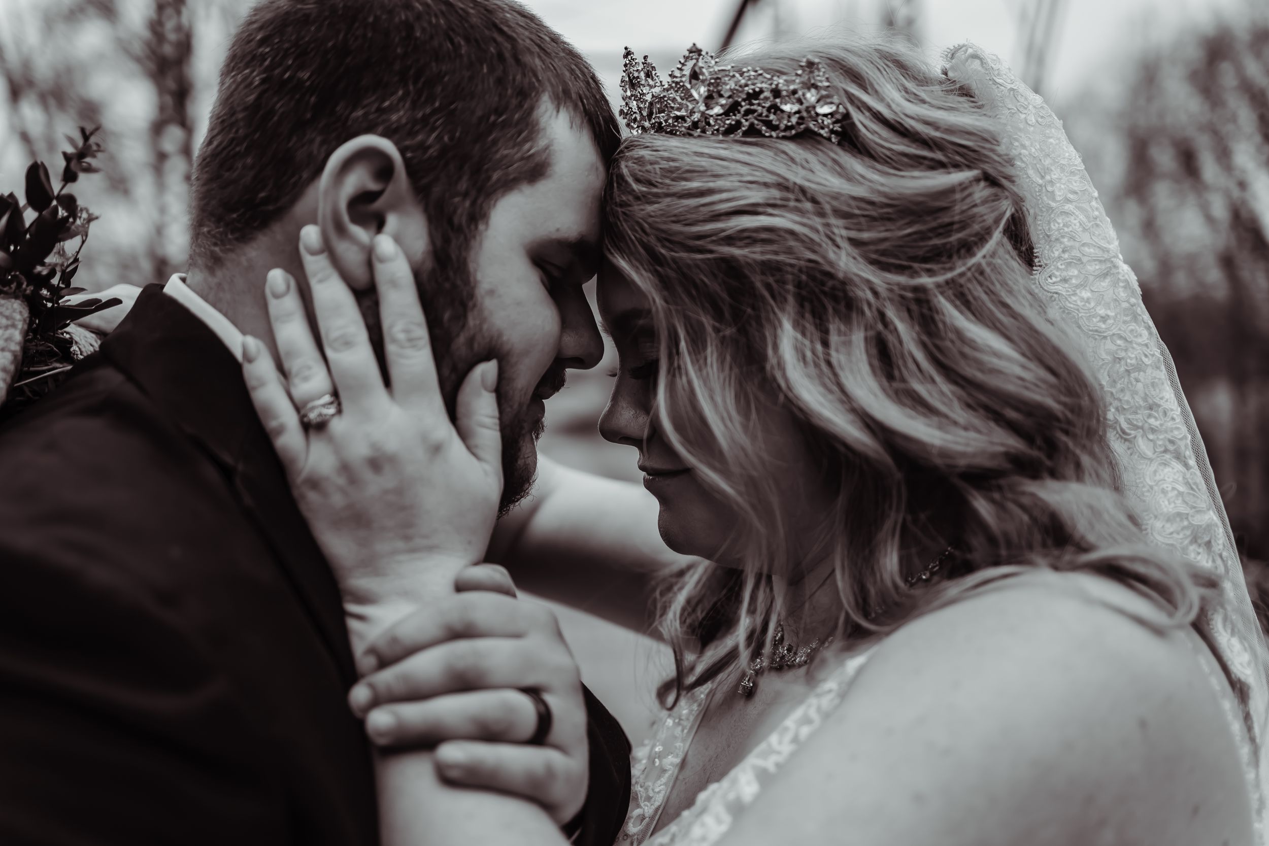 Intimate monochrome portrait of newlywed couple sharing tender moment outdoors during wedding celebration.