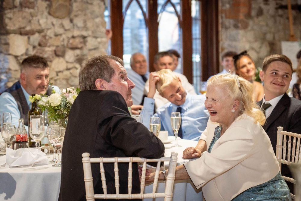 Wedding guests enjoying dinner service in rustic stone venue with natural window lighting.