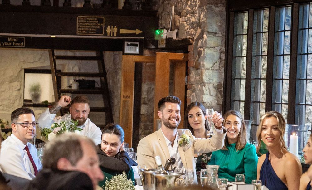 Wedding guests laughing and enjoying drinks at a rustic stone venue during a reception celebration.