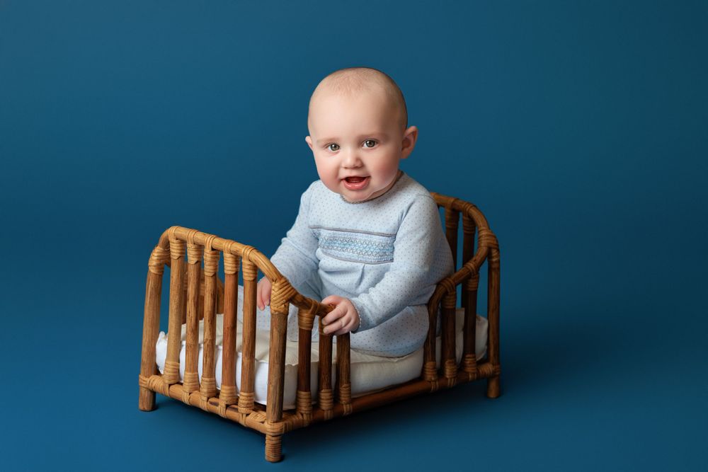 Small wicker crib with light blue backdrop for baby photography session.