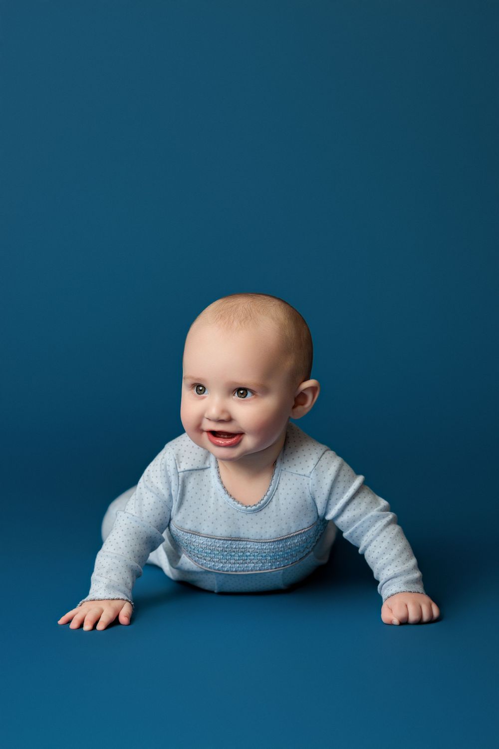 Baby wearing blue knit sweater crawling against deep blue studio backdrop.