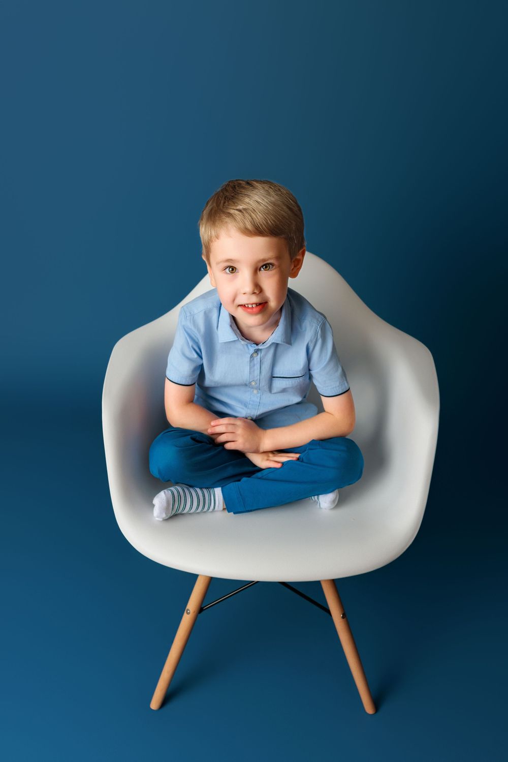 Modern white Eames-style chair with wooden legs against blue backdrop in studio setting.