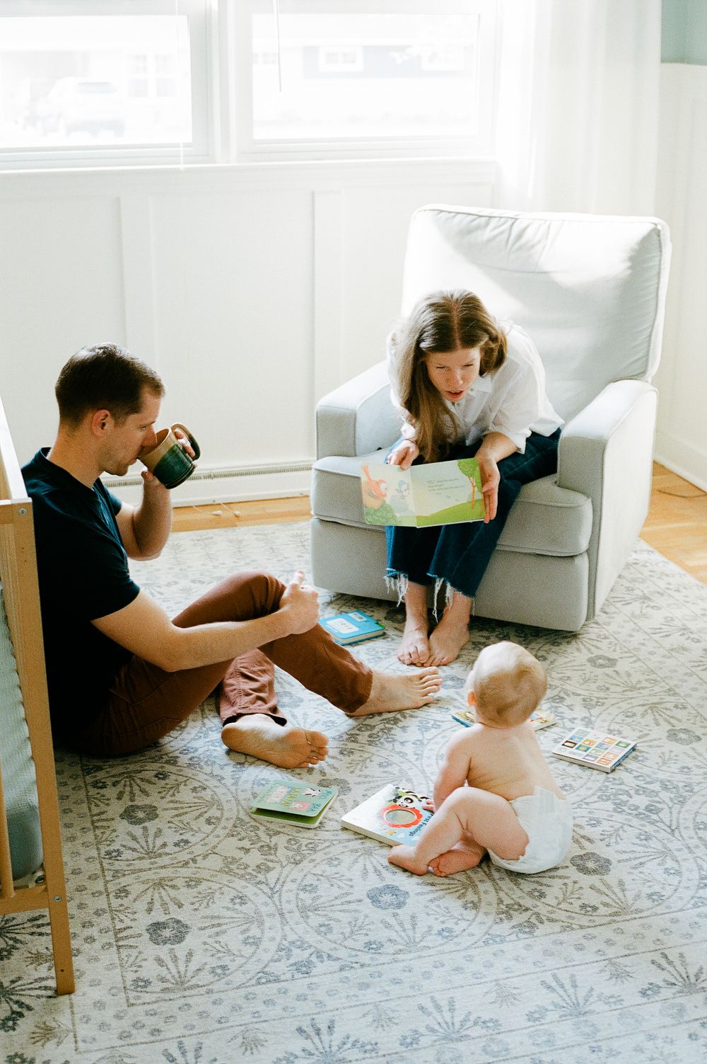 Family reading time together on a patterned rug in a bright room with a cozy armchair.