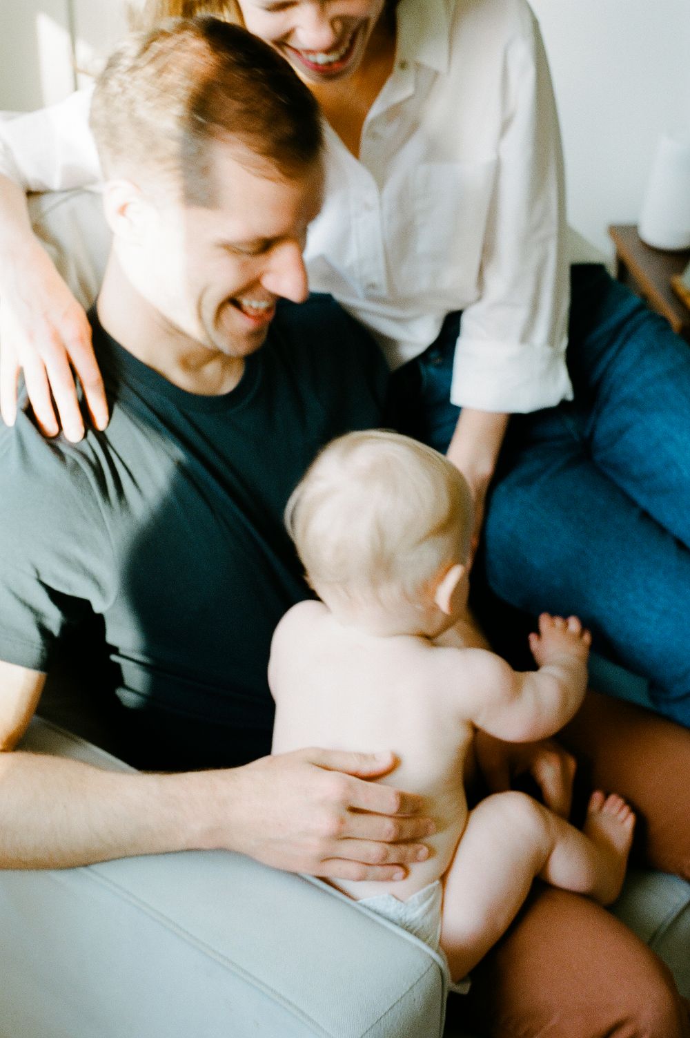 A tender family moment on a light colored couch as parents share loving interactions with their infant child.