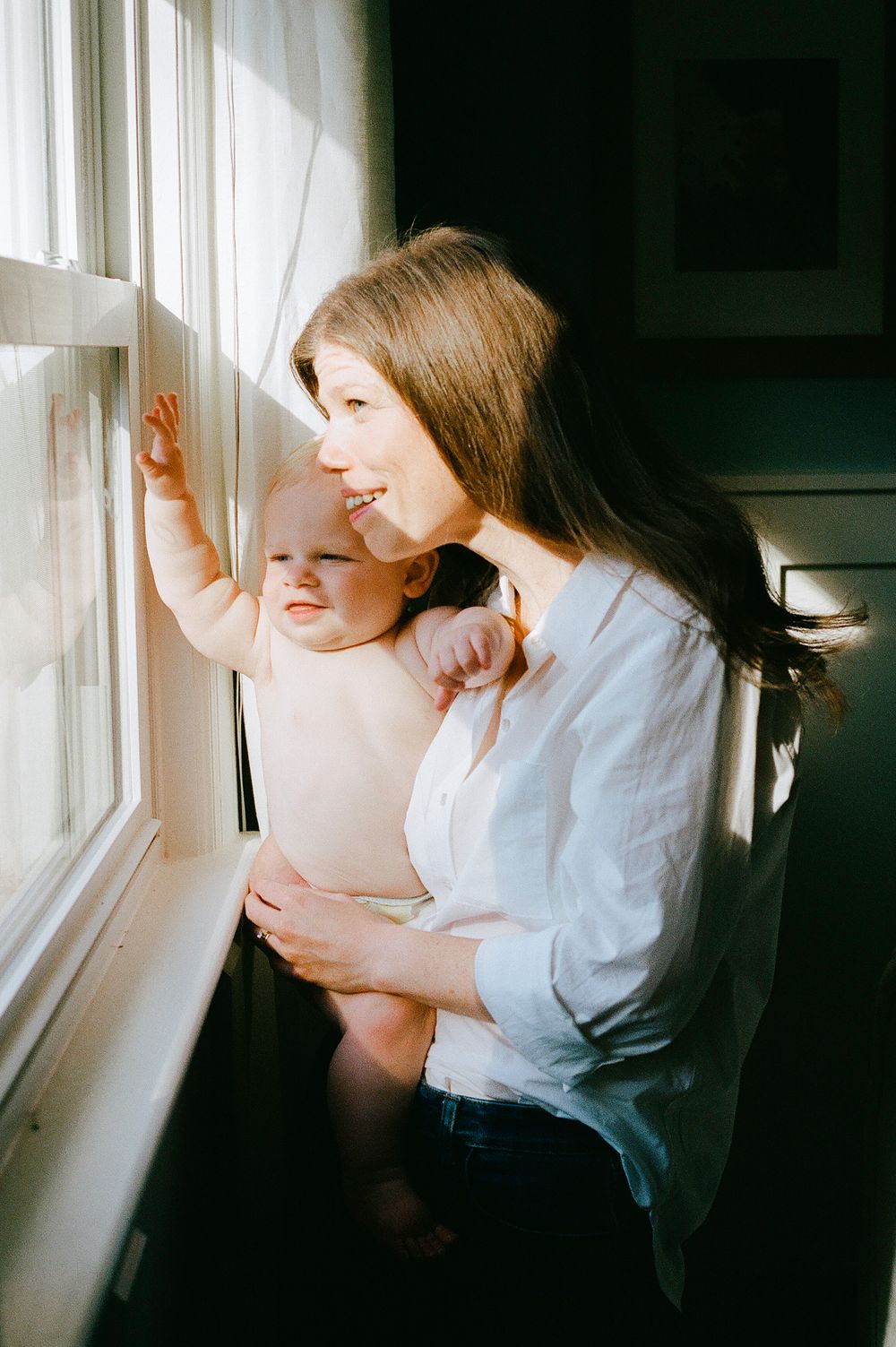 Sweet moment by the window as a caregiver holds a curious baby looking outside.