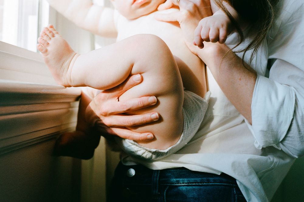 Intimate close-up shot of hands grasping legs and denim while sitting in sunlit window light.