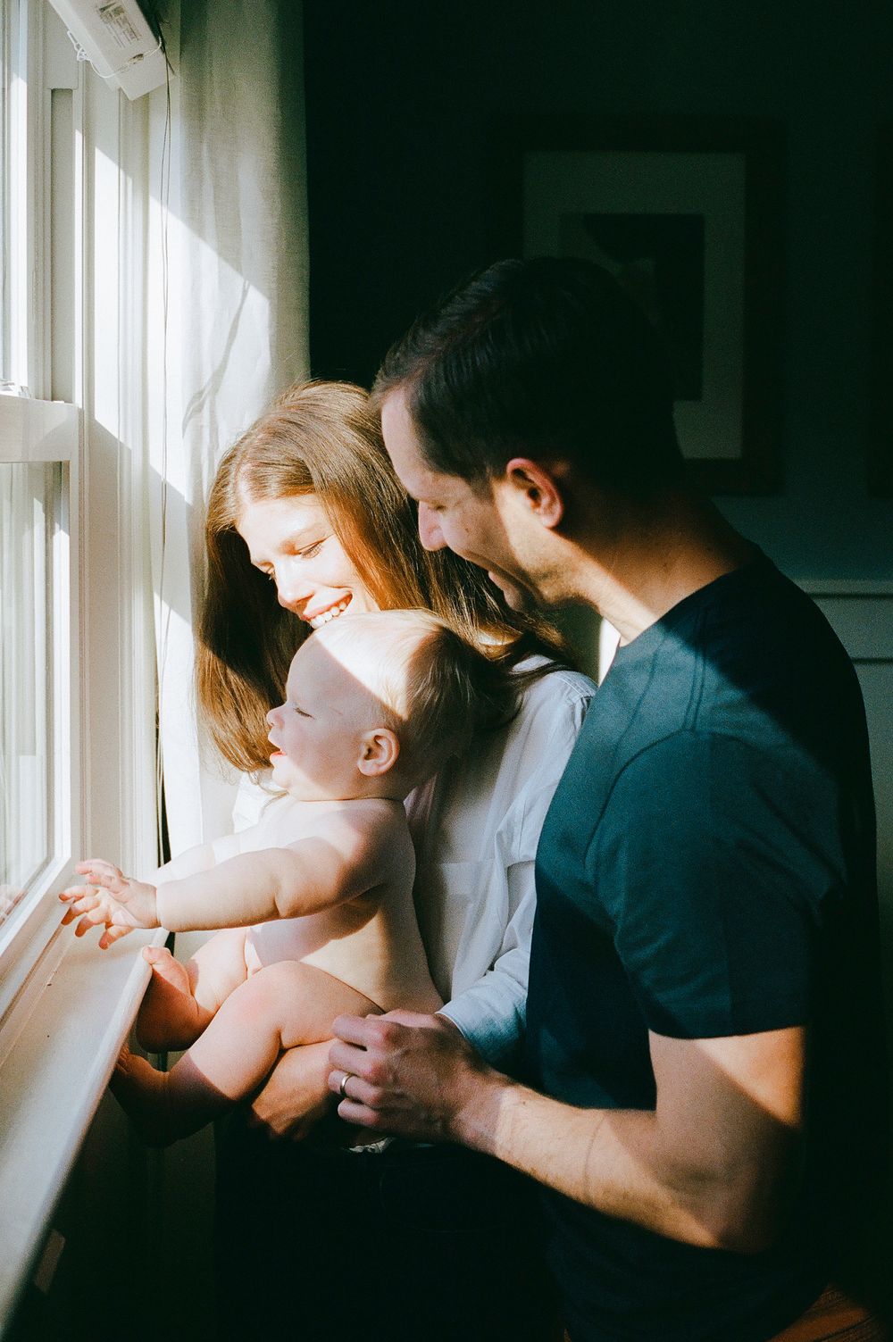 A tender family moment by a sunlit window as parents share a loving moment with their baby.
