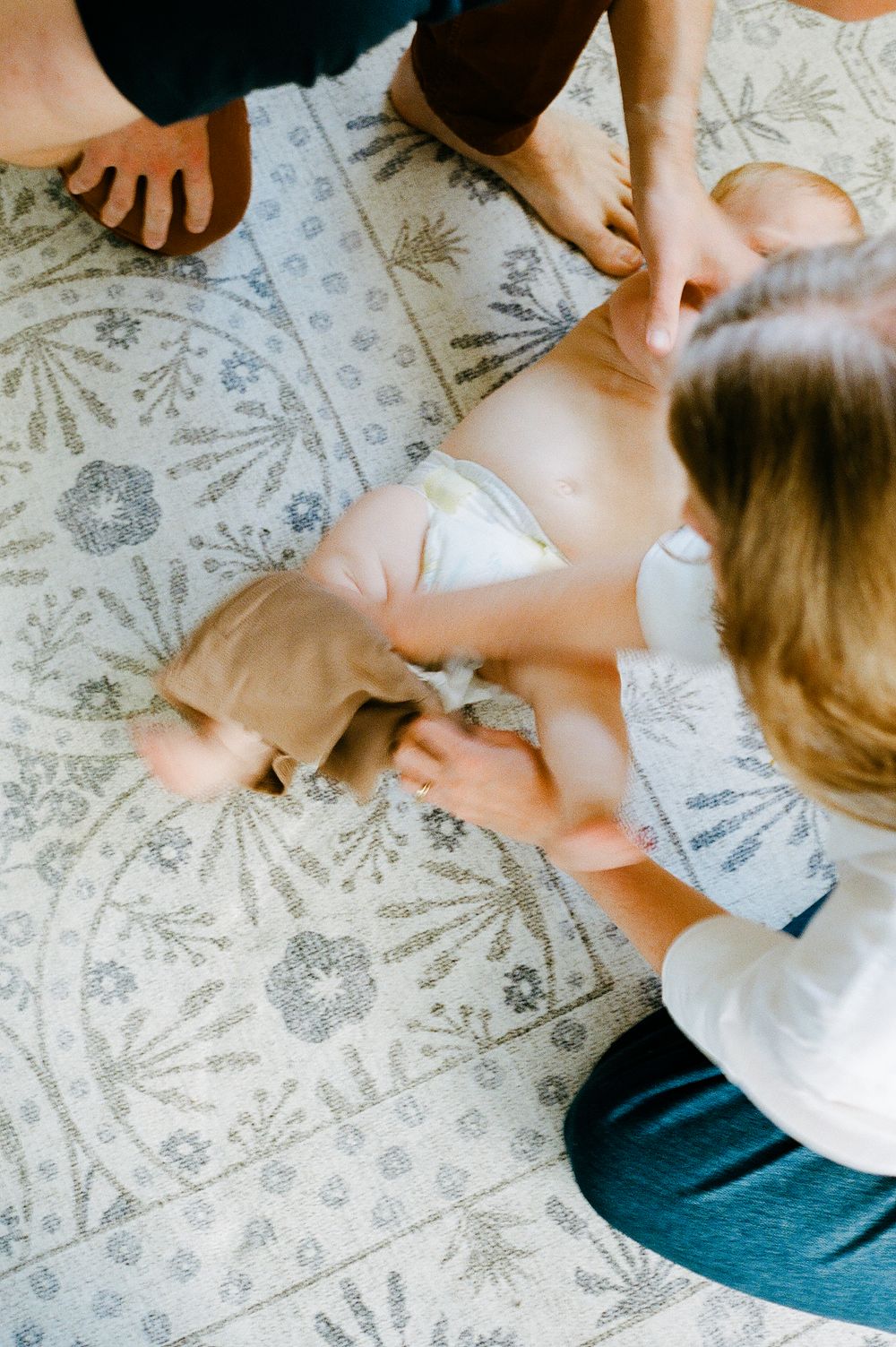 Family playing together on patterned rug during diaper change.