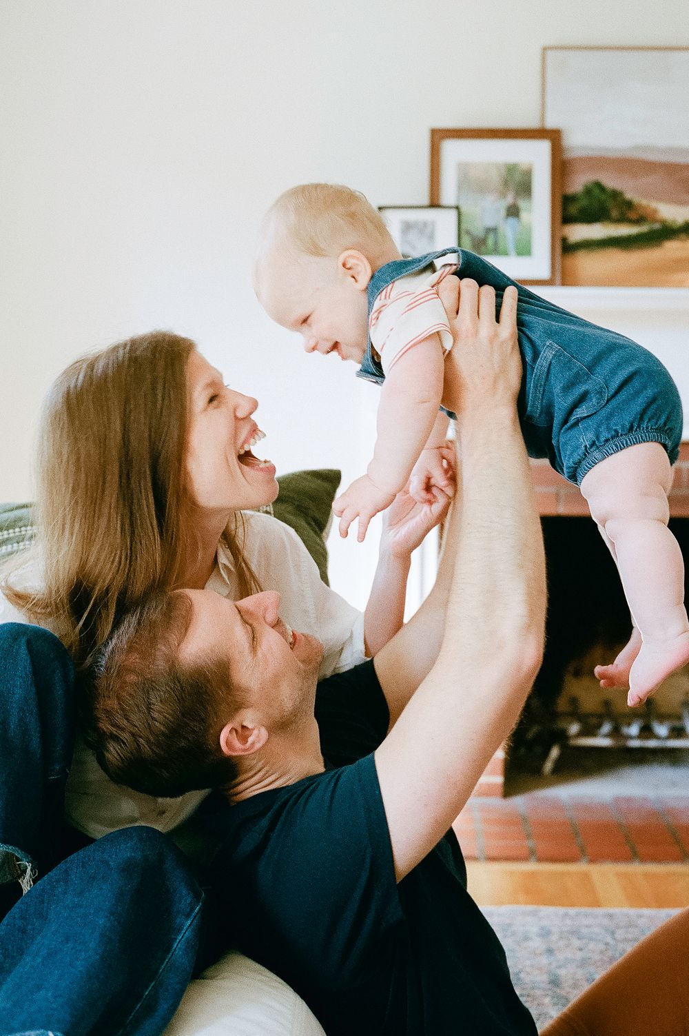 A joyful family moment with parents lifting their baby up high while laughing together in their living room.