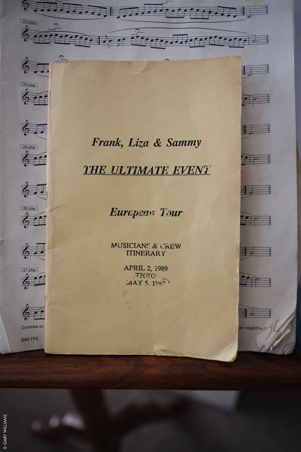 A vintage musicians' and crew itinerary booklet for 'The Ultimate Event' European tour sits against sheet music background.