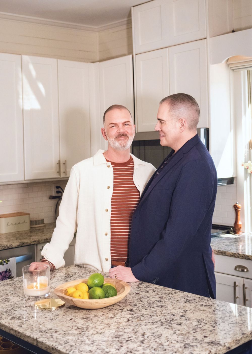 Two people having an intimate conversation while standing in a modern kitchen with granite countertops and citrus fruits.