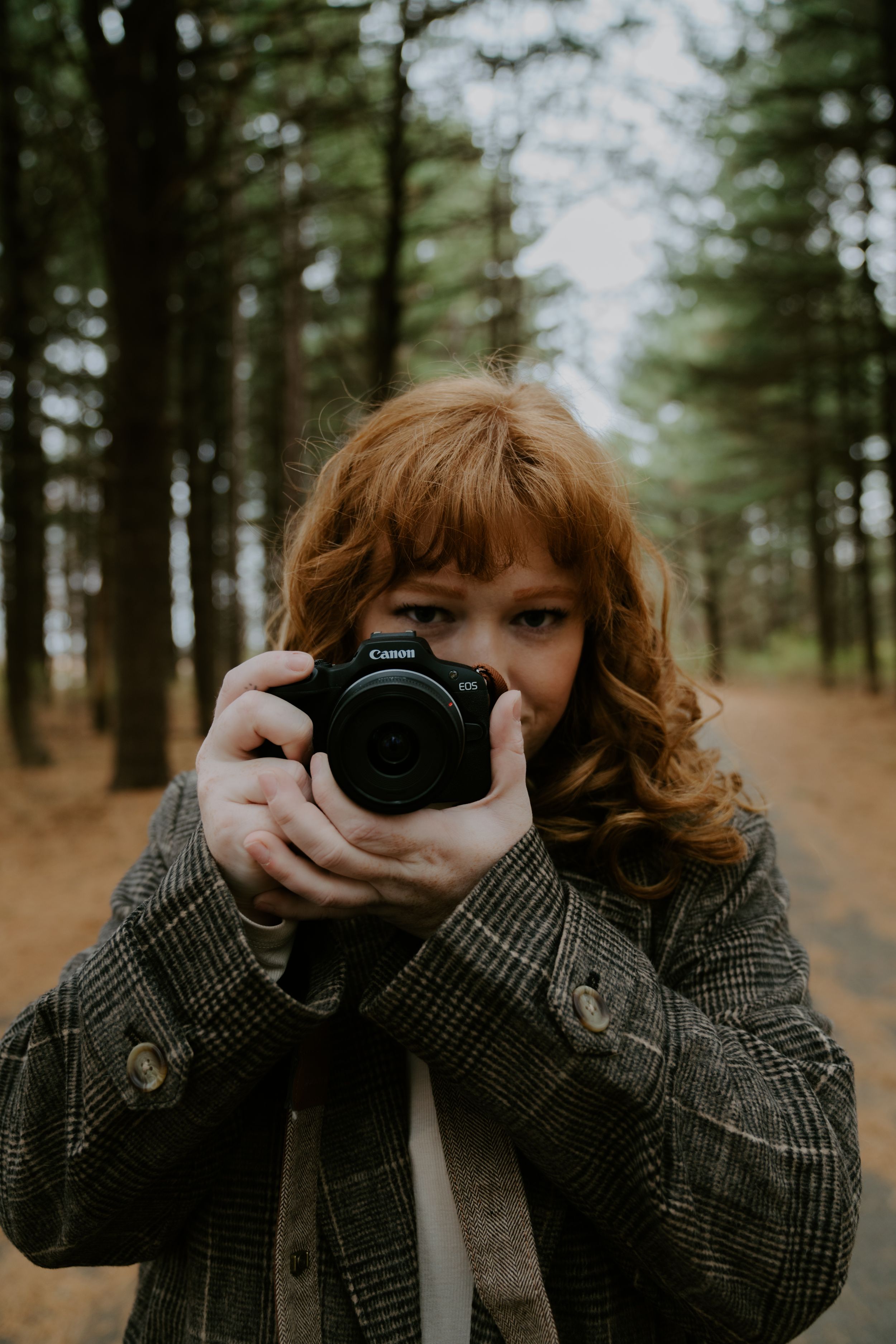 Photographer holding a Canon camera in a forest setting wearing a plaid coat.