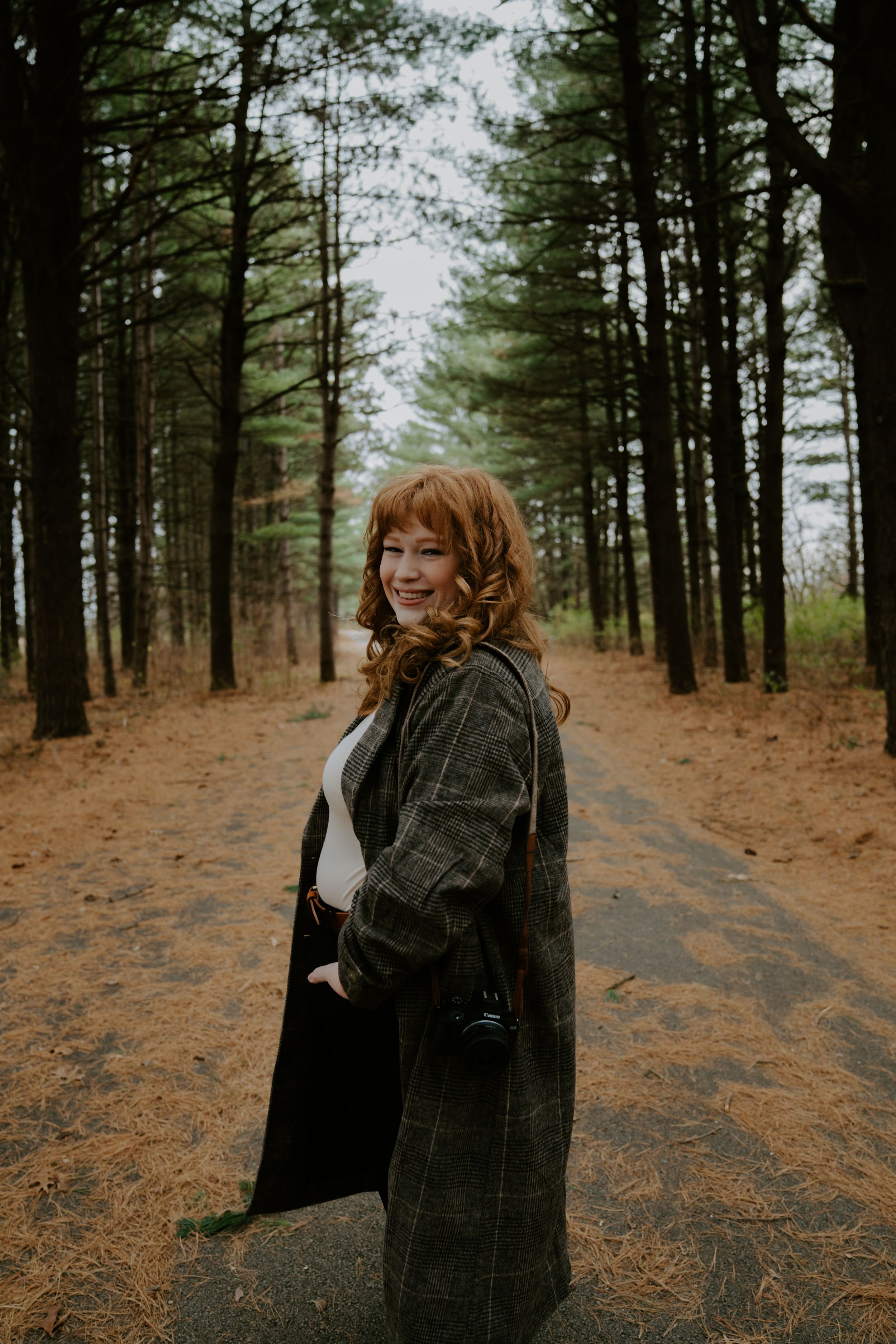 Person in a plaid coat walking through a pine forest path on an autumn day.